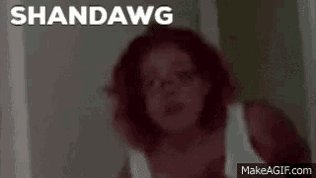 a woman in a white tank top is standing in a doorway with the words shandawg written on the bottom .