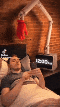 a man is laying in bed with a clock that says 12:00 am on it