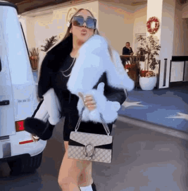 a woman wearing sunglasses and a fur coat is holding a purse