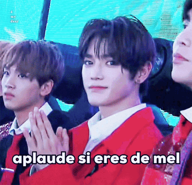 a young man in a red jacket is sitting next to another young man with a caption that says aplaude si eres de mel