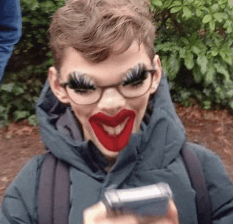 a young boy wearing glasses and fake eyelashes is holding a cell phone and smiling .