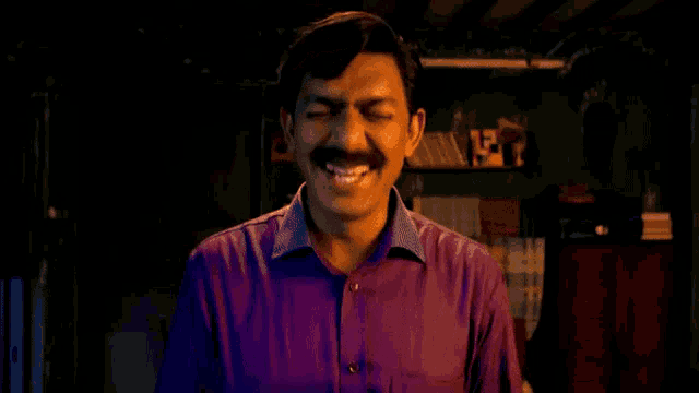 a man in a purple shirt with a mustache is laughing