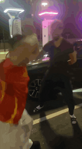 two people are dancing in a parking lot with a purple light behind them