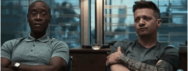 two men are sitting next to each other with their arms crossed in a room .