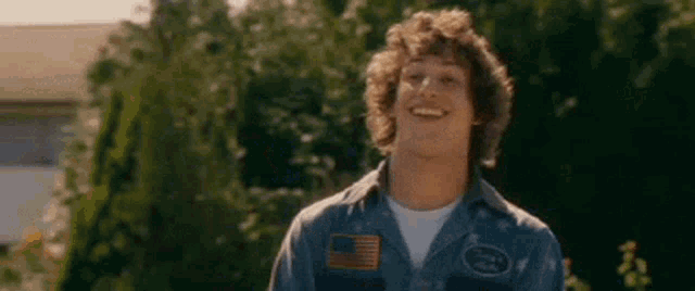 a young man with curly hair is wearing a blue shirt with an american flag on it and smiling .