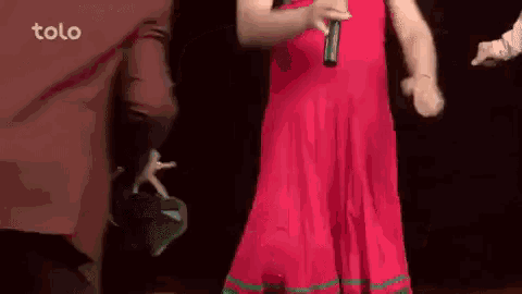 a woman in a red dress is holding a microphone while dancing on a stage .