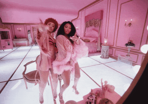 two women are dancing in a pink room with a mirror