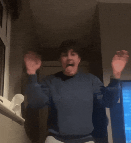 a man in a blue sweater is dancing in a room