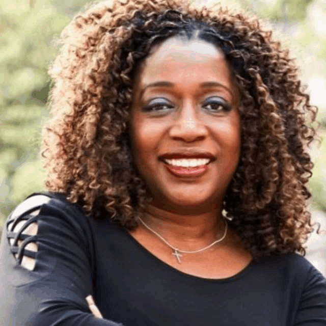 a woman with curly hair is smiling and wearing a black shirt .