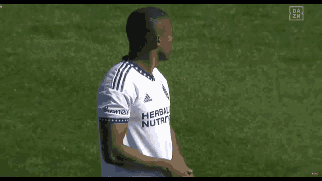 a soccer player wearing a herbal nutrition shirt stands on the field