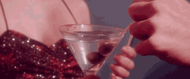 a woman in a sequined dress is holding a martini with olives in it .