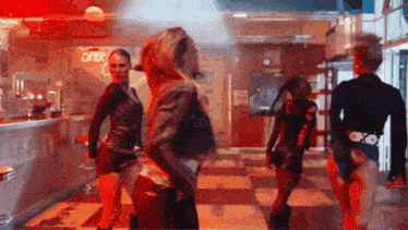 a group of women are dancing in a room with a red exit sign in the background