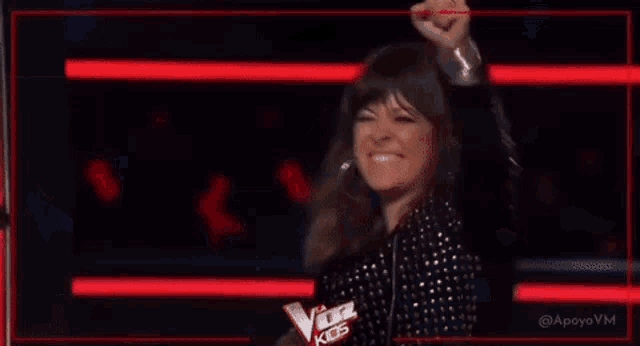a woman is standing on a stage with her fist in the air and holding a sign that says the voice kids .