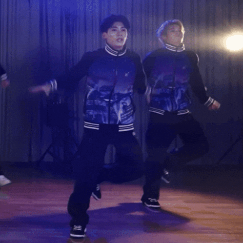 a group of young men are dancing on a stage with a blue curtain behind them