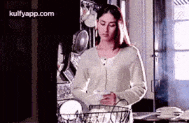 a woman is standing in a kitchen holding a basket of dishes and plates .