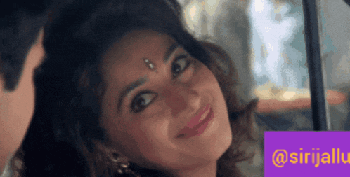 a woman with a bindi on her forehead smiles while looking out a car window