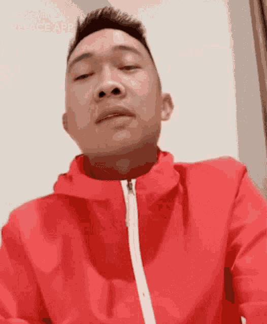 a man wearing a red jacket with a white zipper looks at the camera