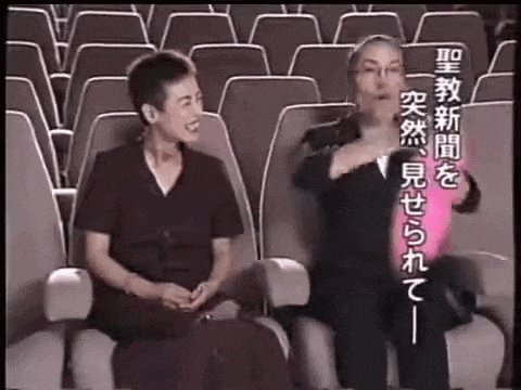 two women are sitting in a theater talking to each other while holding balloons .