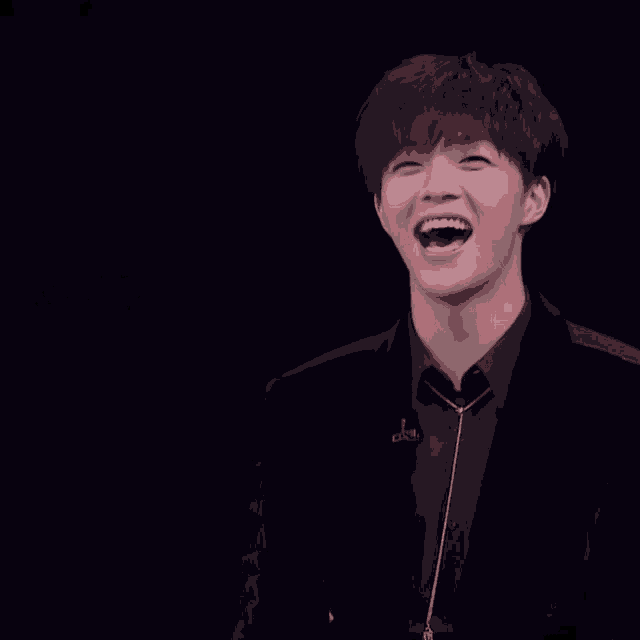 a man in a black suit is laughing in front of a black background with chinese writing
