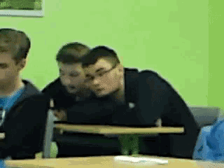a group of young men are sitting at a table with a green wall behind them