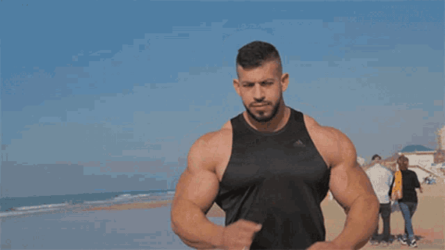a man wearing a black adidas tank top is running on a beach
