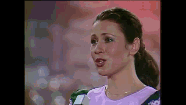 a woman in a purple shirt is talking into a microphone