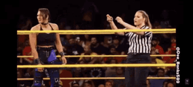 two women are standing in a wrestling ring and one is wearing a striped shirt