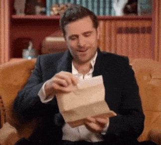 a man in a suit is sitting in a chair holding a piece of paper in his hands .