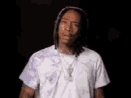 a man with dreadlocks is wearing a white t-shirt and a purple tie dye jacket .