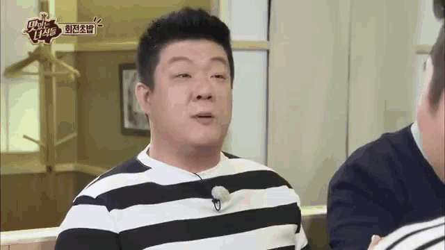 a man in a striped shirt is talking to another man in a room .