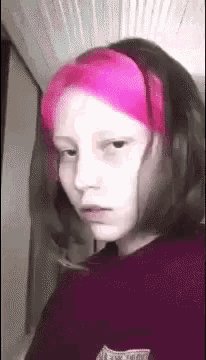 a young girl with pink hair is making a funny face while wearing a headband .