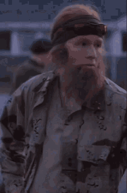 a man with a beard is wearing a headband and a camouflage shirt