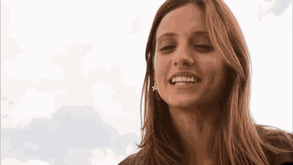 a close up of a woman 's face smiling with a cloudy sky in the background