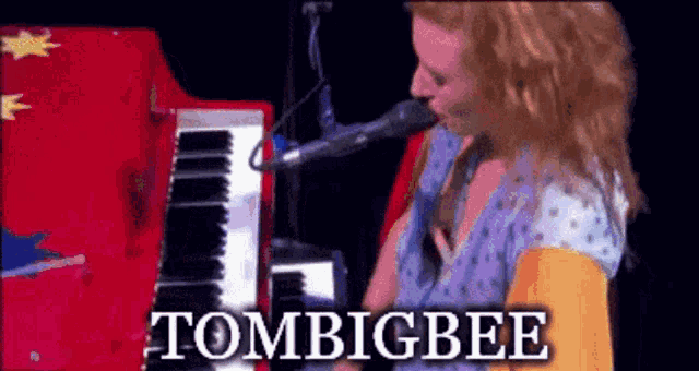 a woman is singing into a microphone while playing a red piano with the words tombigbee written on the bottom