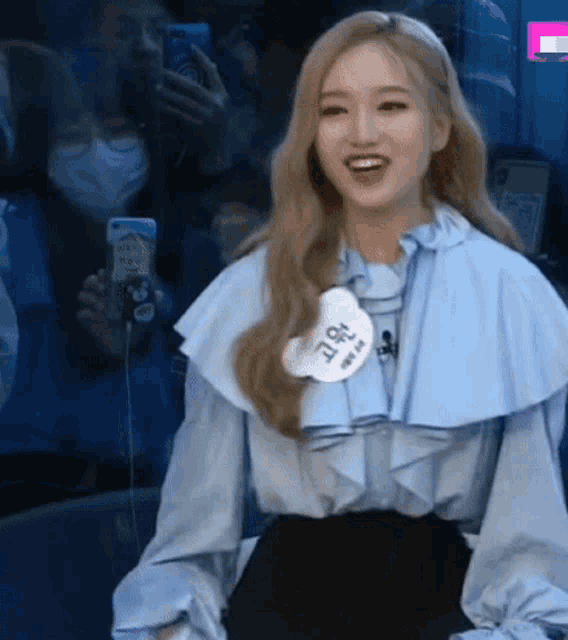 a woman wearing a blue ruffled blouse with a name tag that says ' a ' on it .