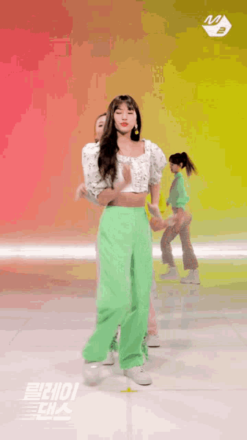 a girl in green pants and a white top is dancing with other girls