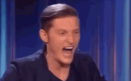 a man is making a funny face while sitting in front of a microphone on a stage .