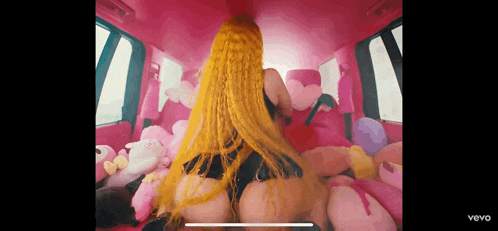a woman with yellow hair is in the back of a pink car surrounded by stuffed animals .