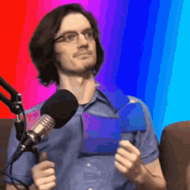 a man wearing glasses is standing in front of a microphone holding a blue item .