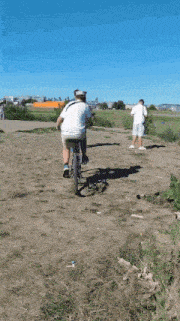 a man riding a bike in a field with a large orange building in the background