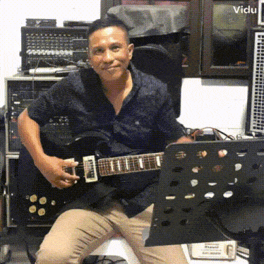 a man in a blue shirt is playing a guitar in front of a music stand