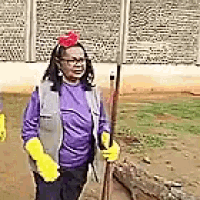 a woman in a purple shirt and yellow gloves is holding a broom in a field .