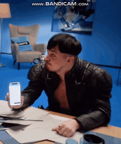 a man sitting at a table holding a cell phone with the website www.bandicam.com visible