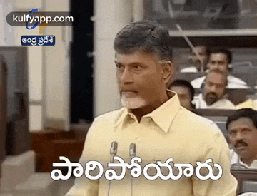 a man in a yellow shirt is giving a speech in front of a crowd in a parliament .