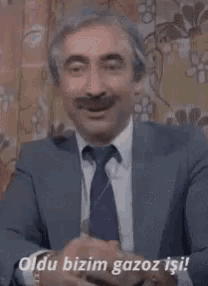 a man with a mustache is wearing a suit and tie and says oldu bizim gazoz isi !