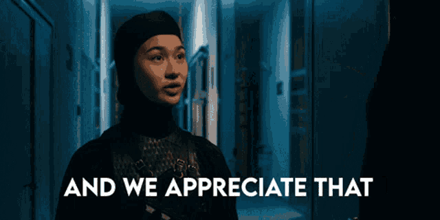 a woman in a hijab is standing in a hallway with the words " and we appreciate that " behind her