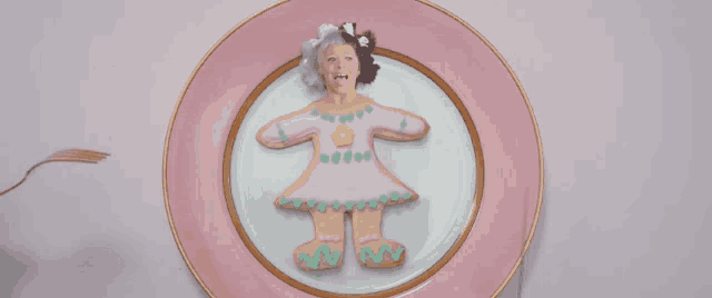 a pink plate with a cookie that looks like a doll on it