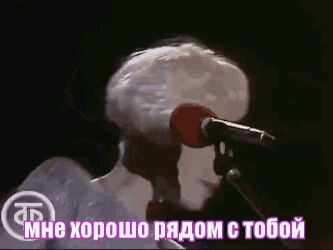 a man is singing into a microphone in a dark room with russian writing behind him .