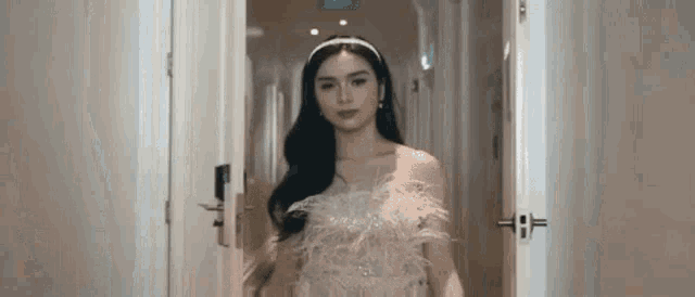 a woman in a feathered dress is standing in a hallway next to a door .