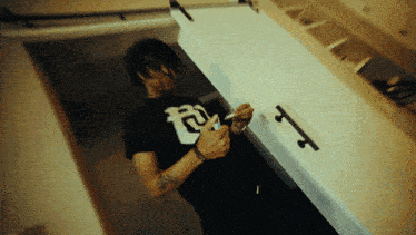 a man wearing a black shirt with the letter t on it is smoking a cigarette